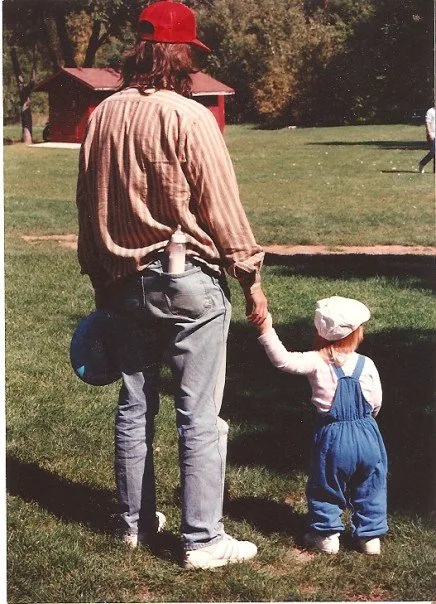 A father and his young child holding hands in a park