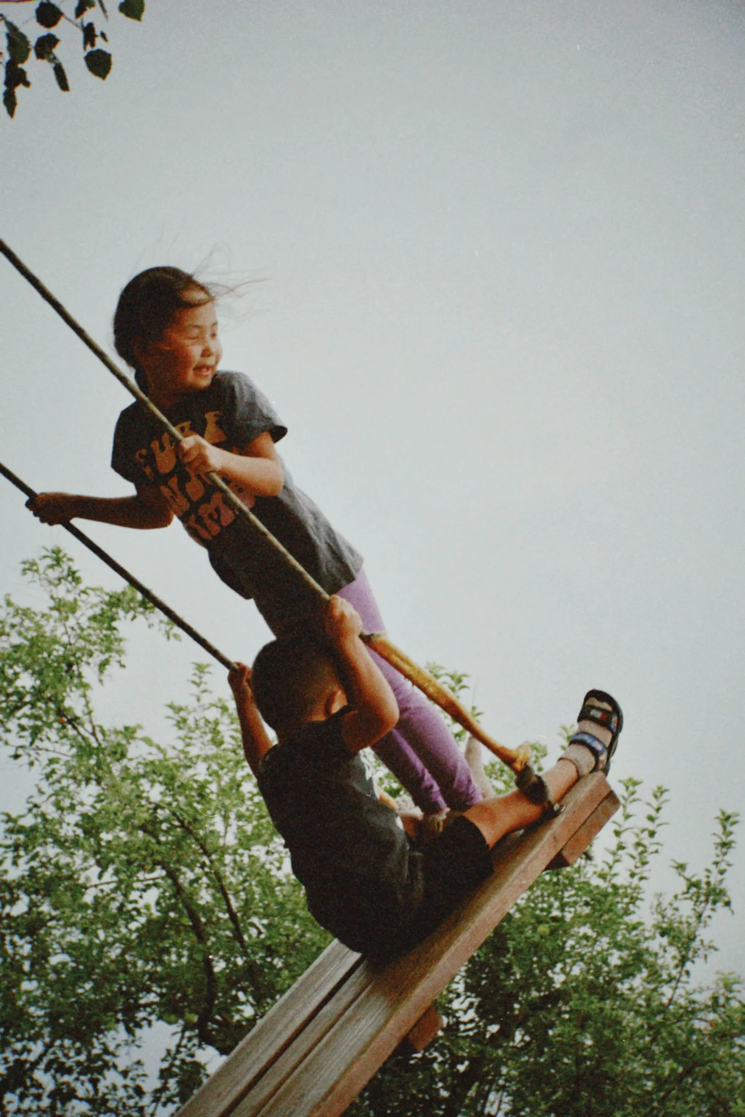 Two children laughing together on a swing at dusk
