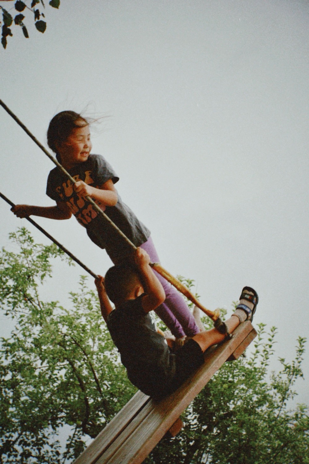 Two children laughing together on a swing at dusk