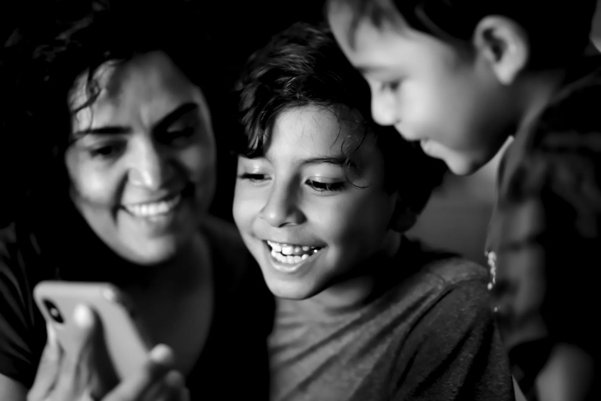 A mother and two sons smiling at a phone together