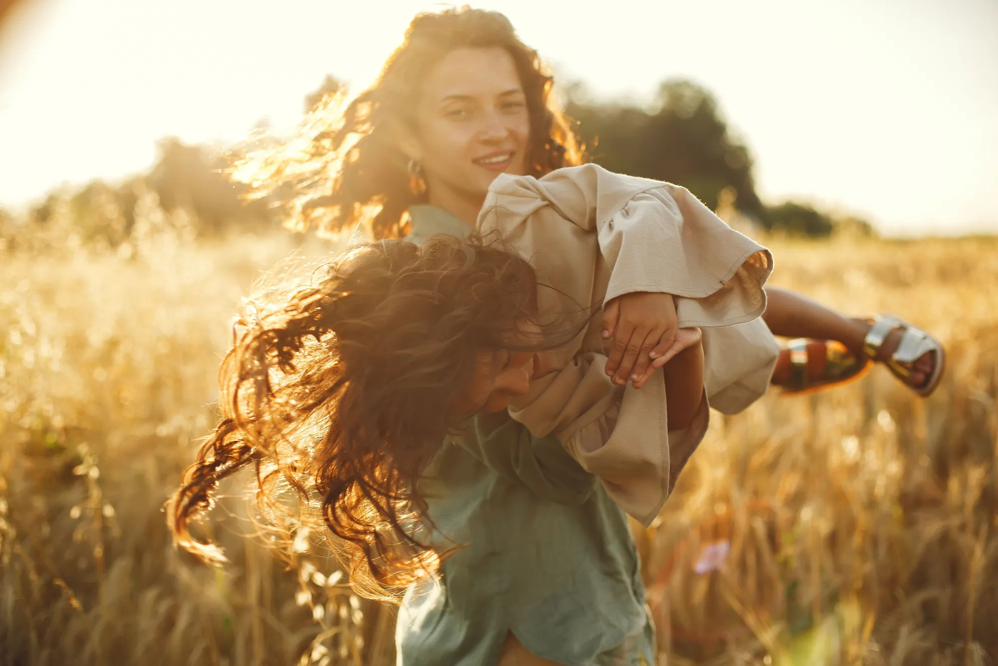 Mother playing with her daughter in a sunlit field at golden hour
